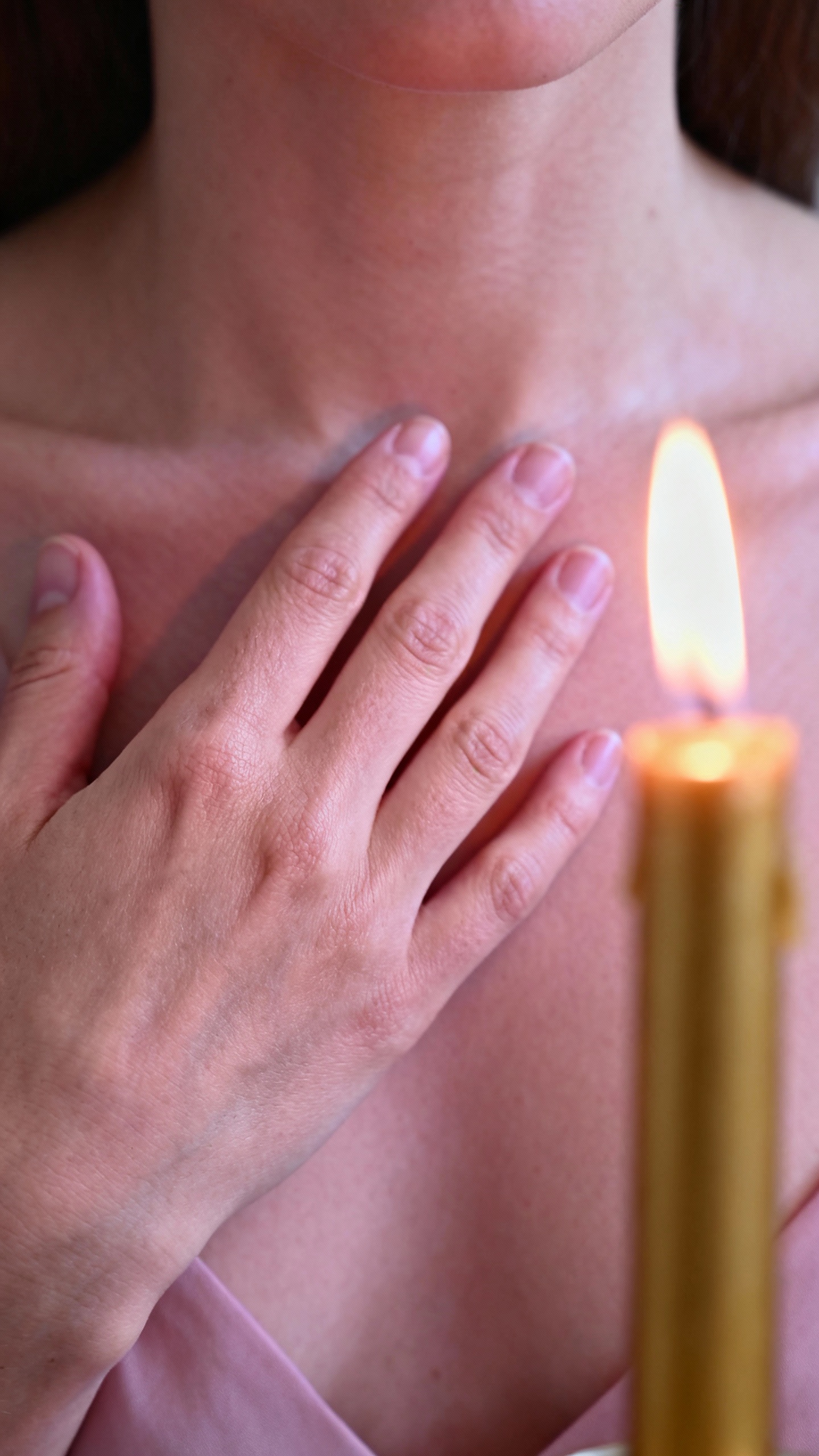 Closeup of female hand over heart, candle flicker, soft pink light