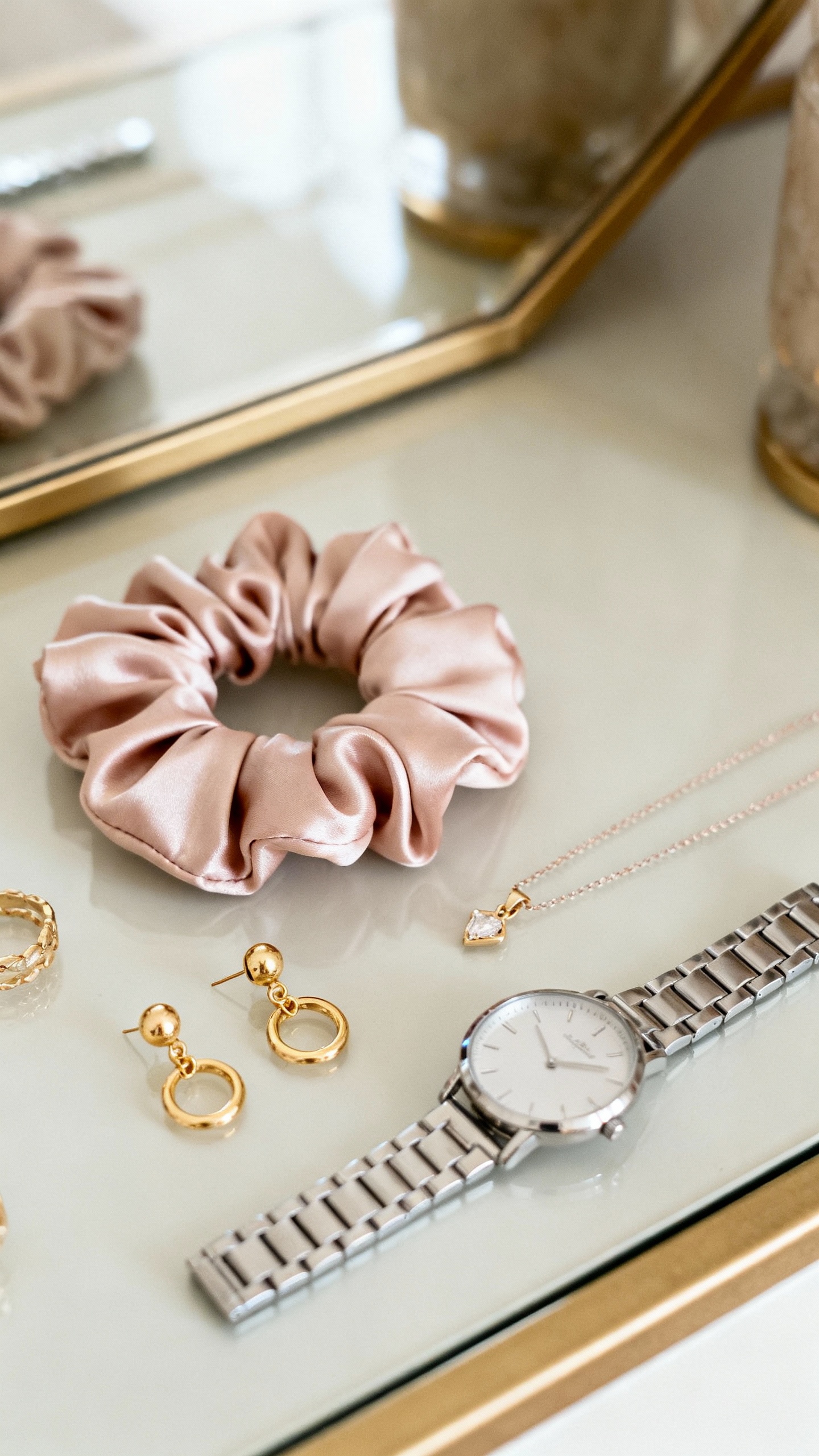 Neatly arranged micro-accessories on vanity: silk scrunchie, delicate necklace, gold earrings, sleek