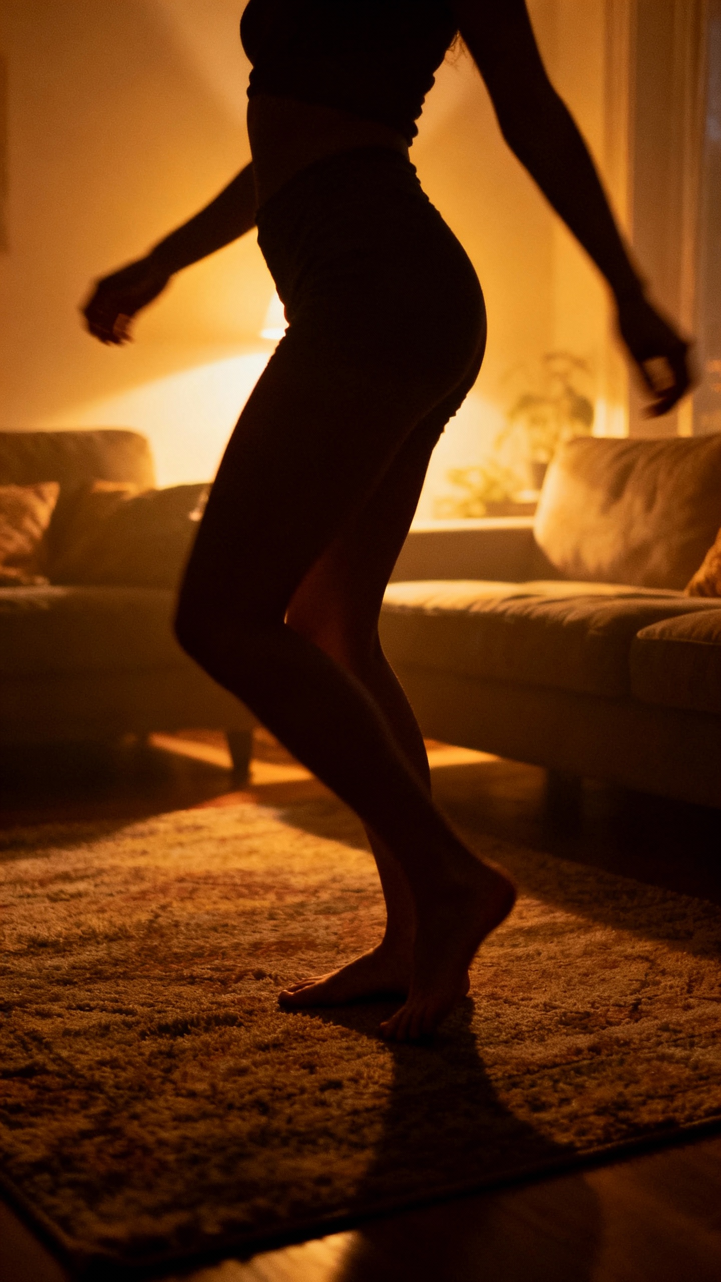 Slow-motion hip sway silhouette in cozy living room, barefoot on rug, evening glow