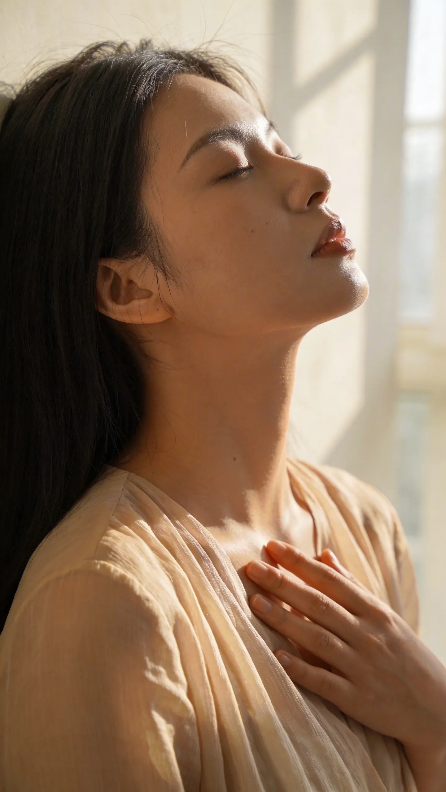 Woman exhaling, hand on heart, soft window light