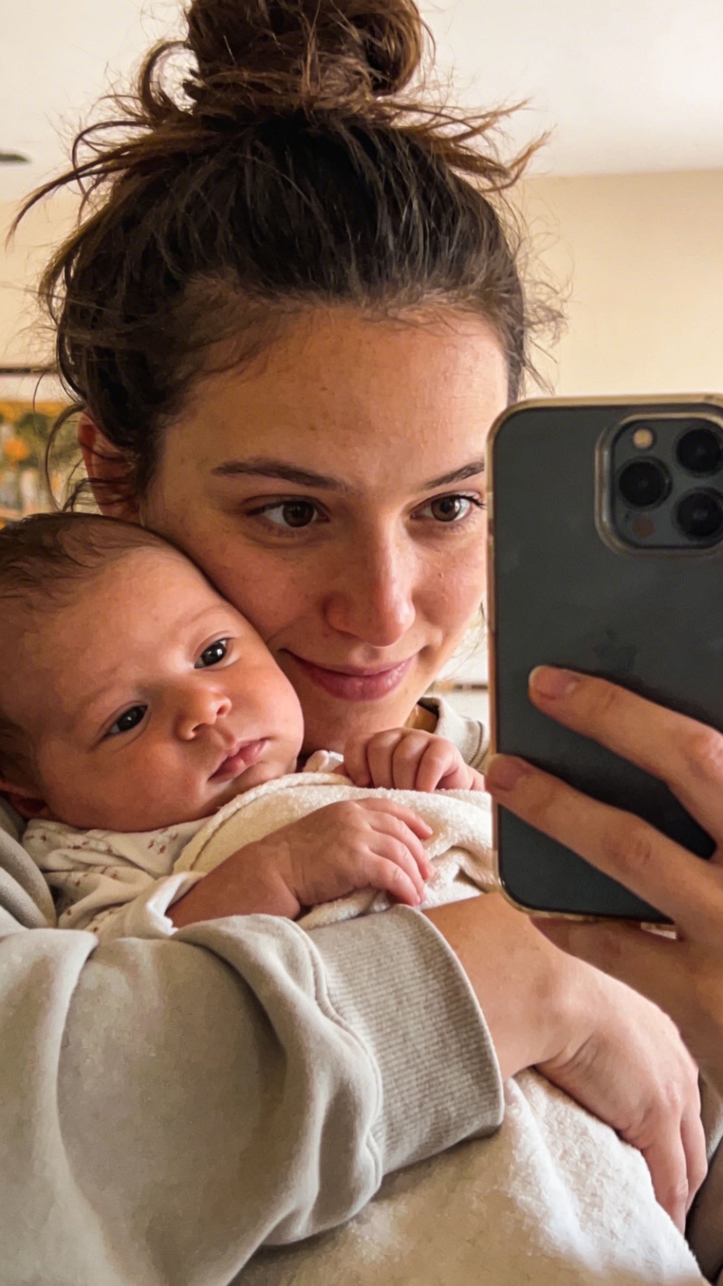 New mom holding baby, mirror selfie, messy bun, soft light