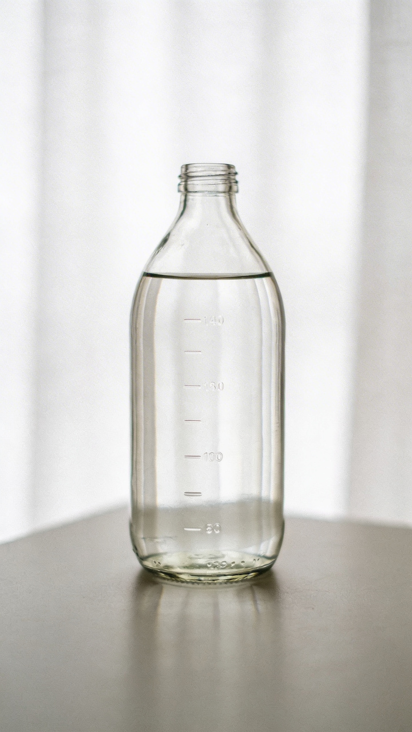 single glass water bottle on desk with time markers, minimal backdrop