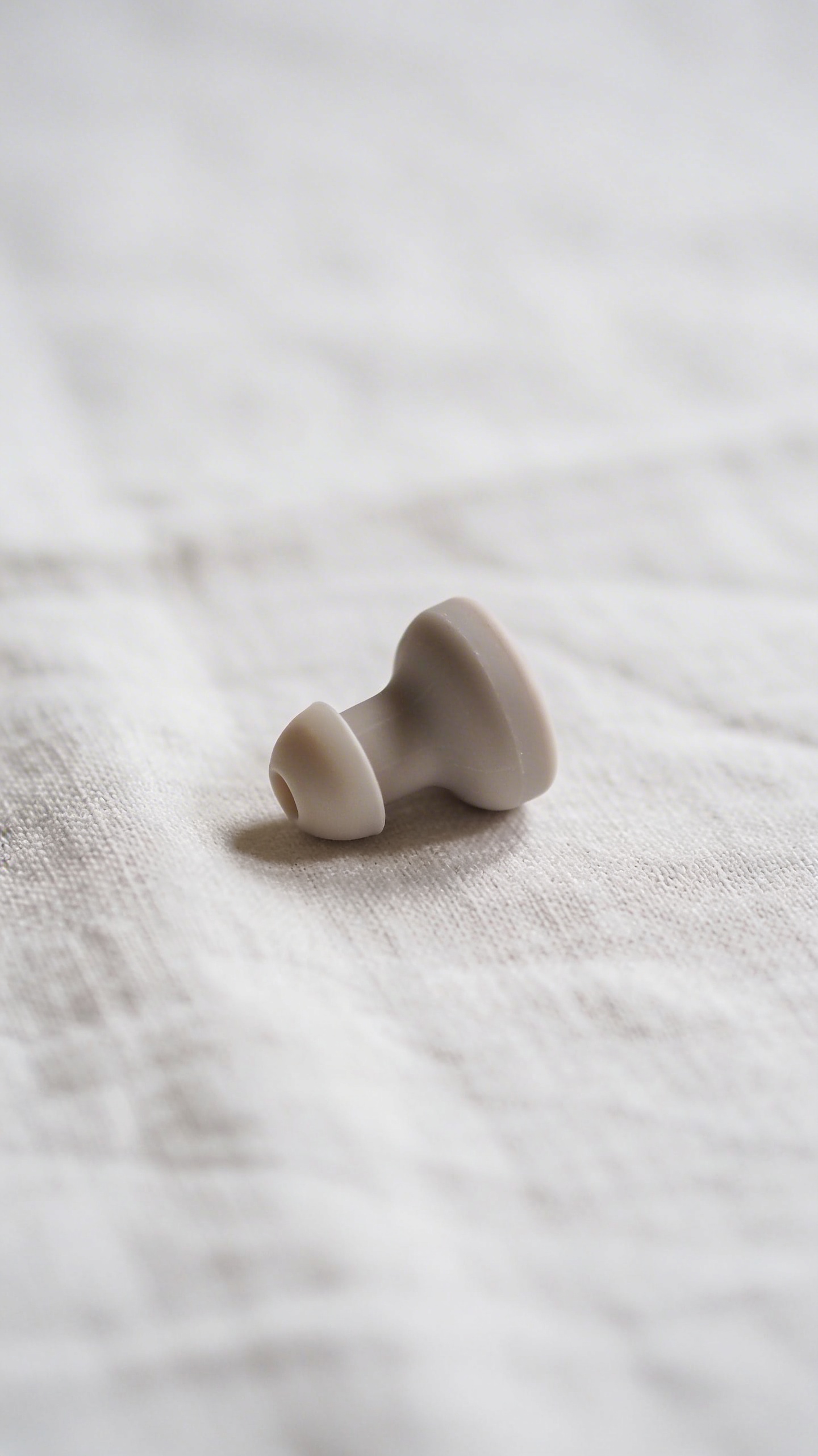 single silicone earplug on white linen surface