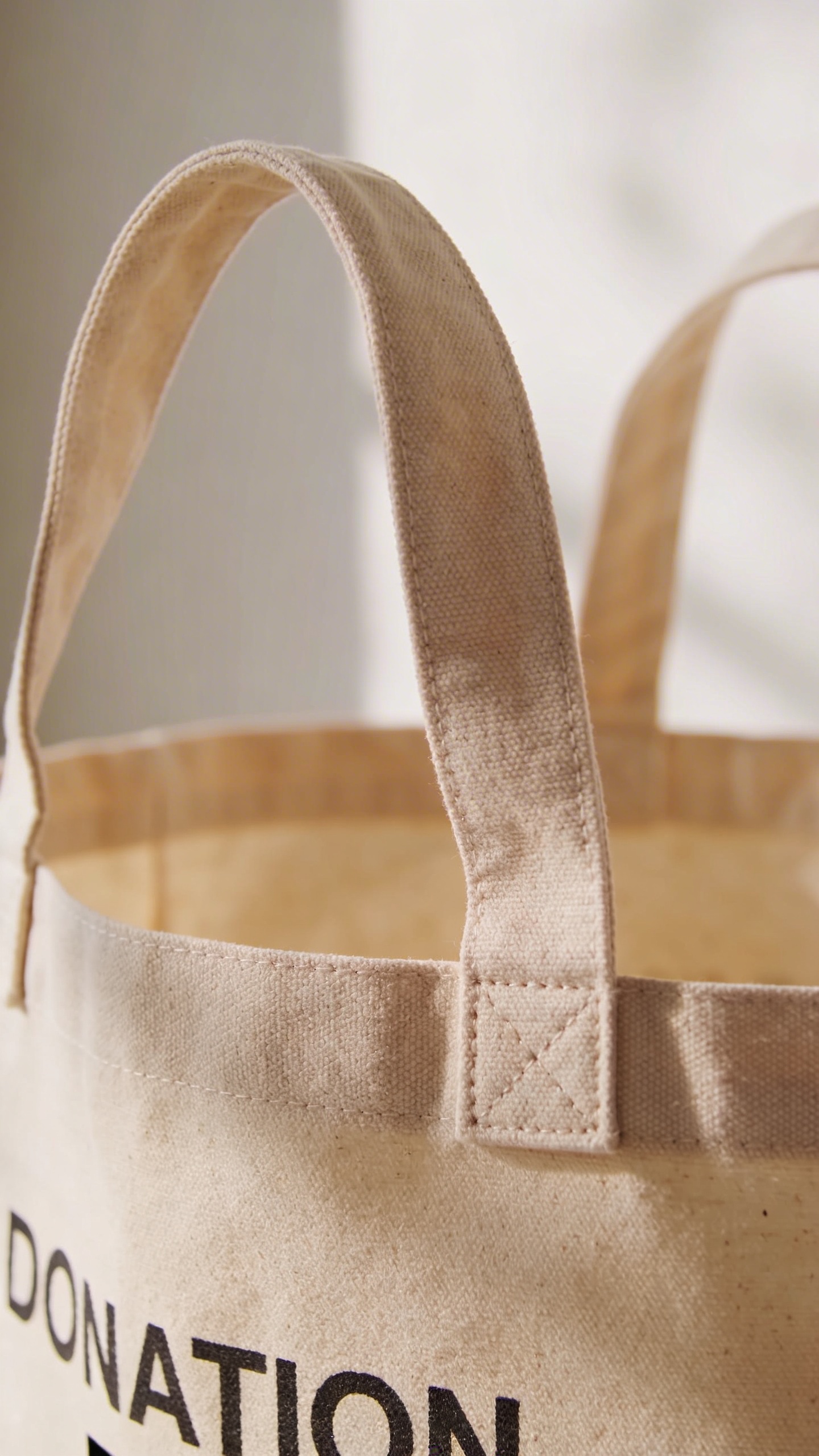 labeled donation tote in beige canvas, closeup handhold handles