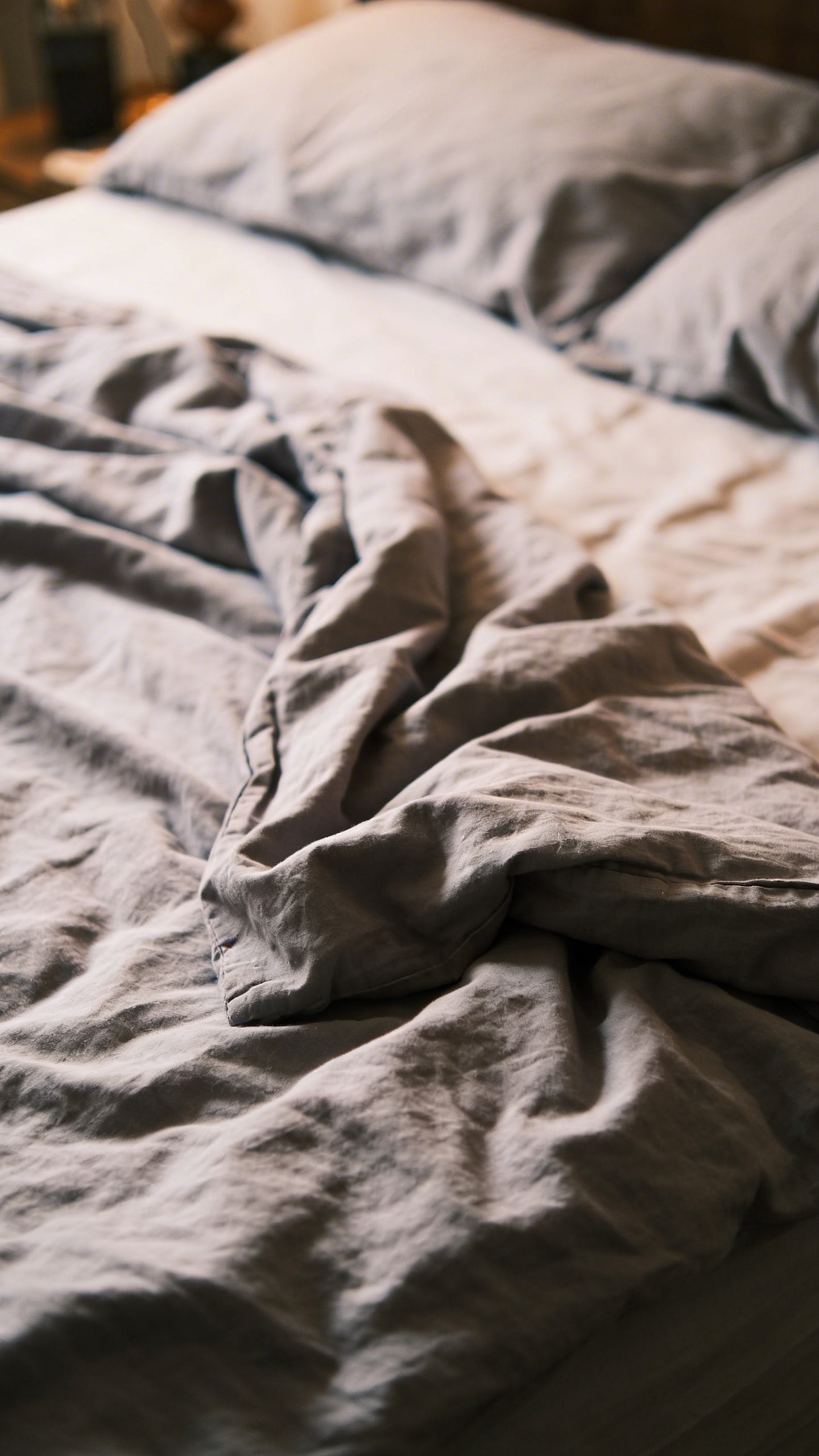 single empty side of a double bed, rumpled gray sheets