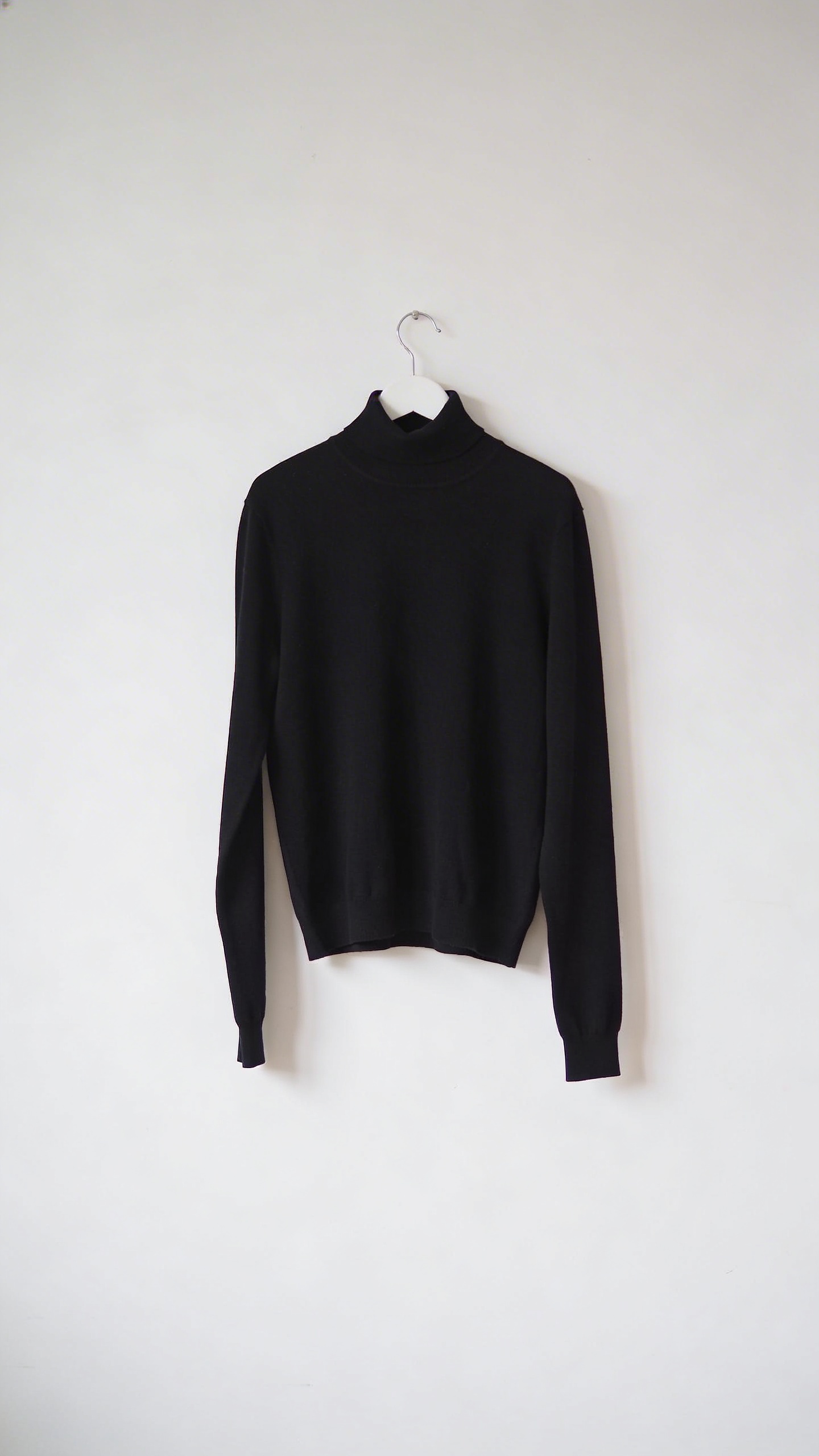 lone black turtleneck on white hanger against blank wall