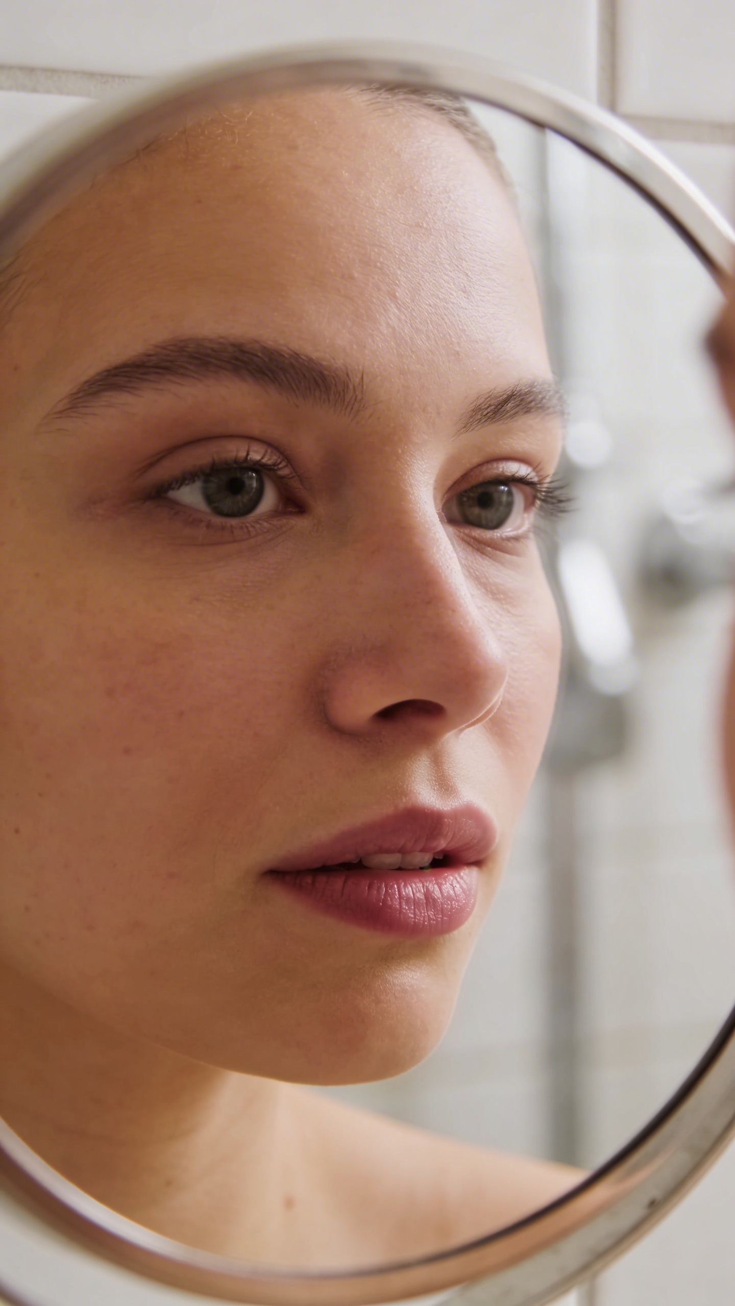 closeup of one woman’s face reflected in bathroom mirror