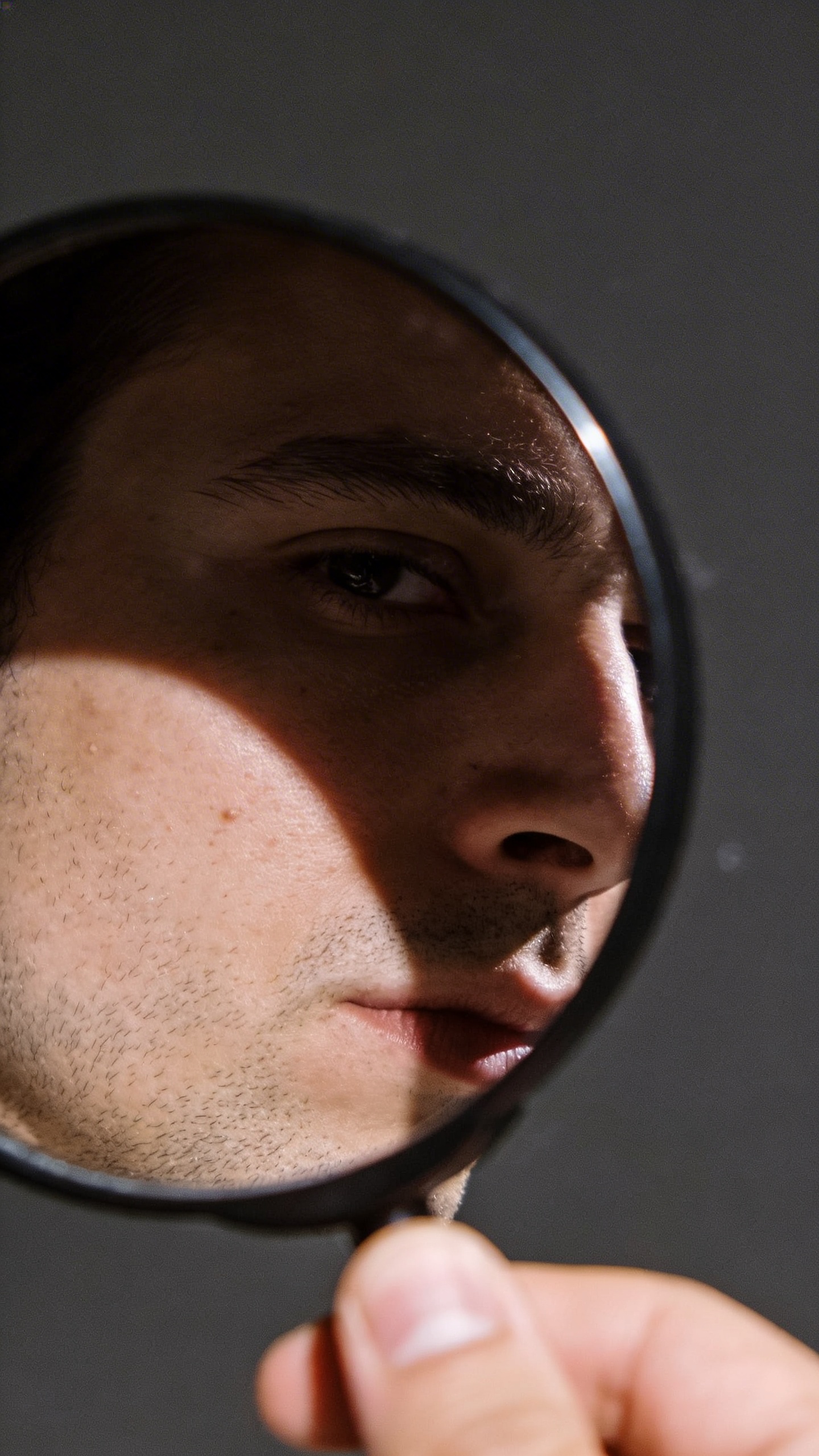 single handheld mirror showing man’s cheek under harsh light